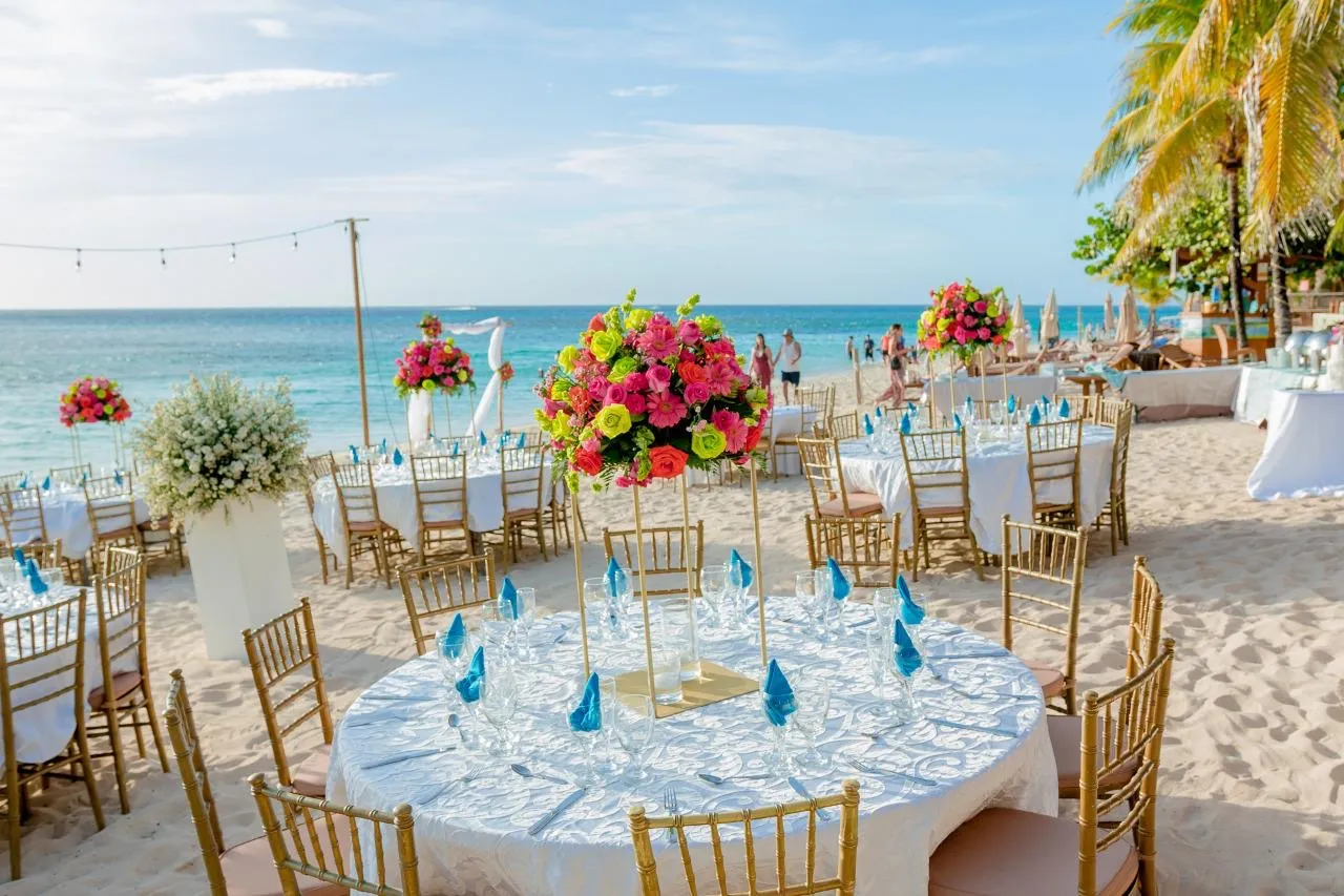 Beach wedding reception tables with tropical centerpieces by the ocean in Roatán