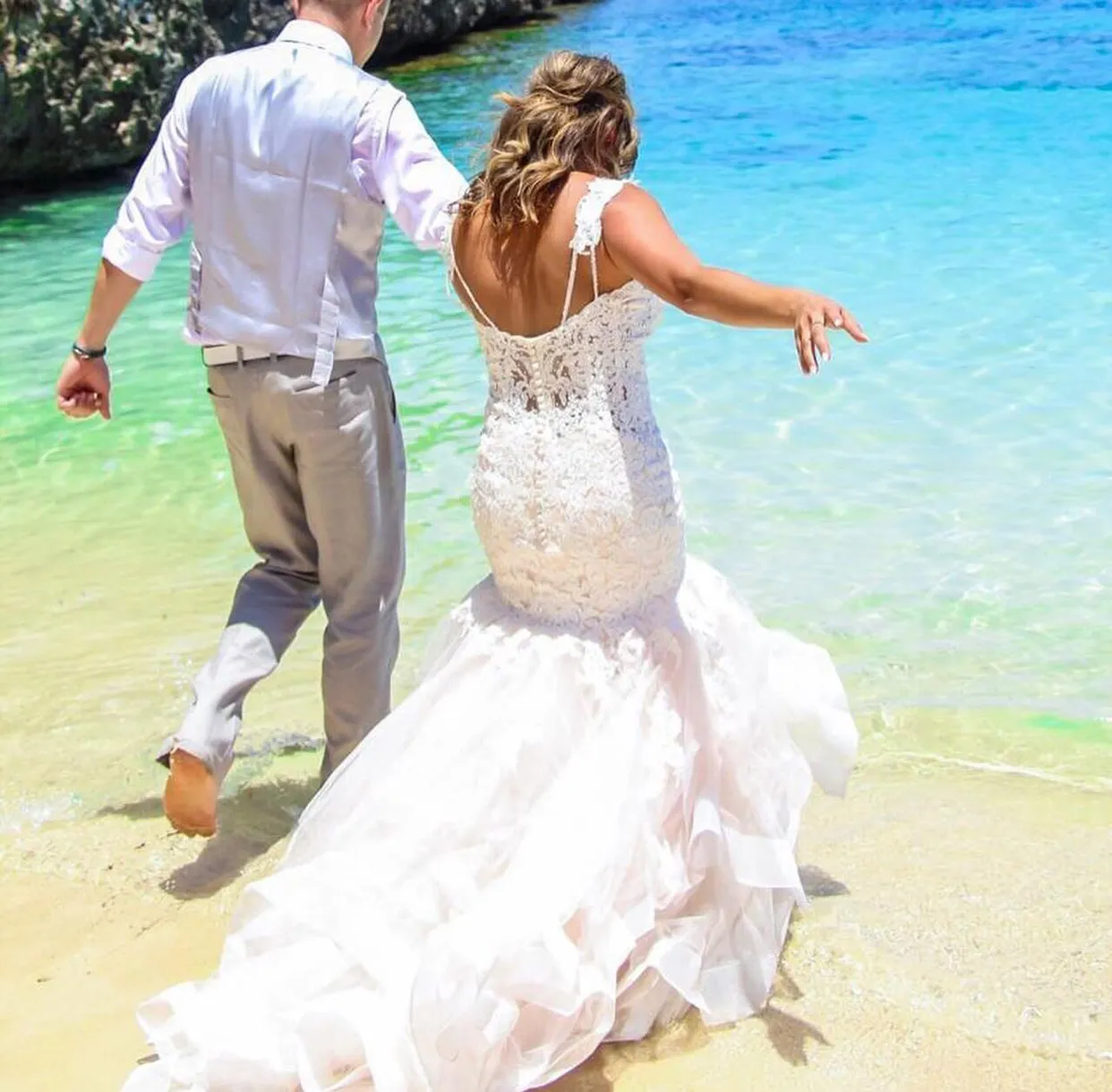 Bride and groom walking hand in hand into clear turquoise water on the beach
