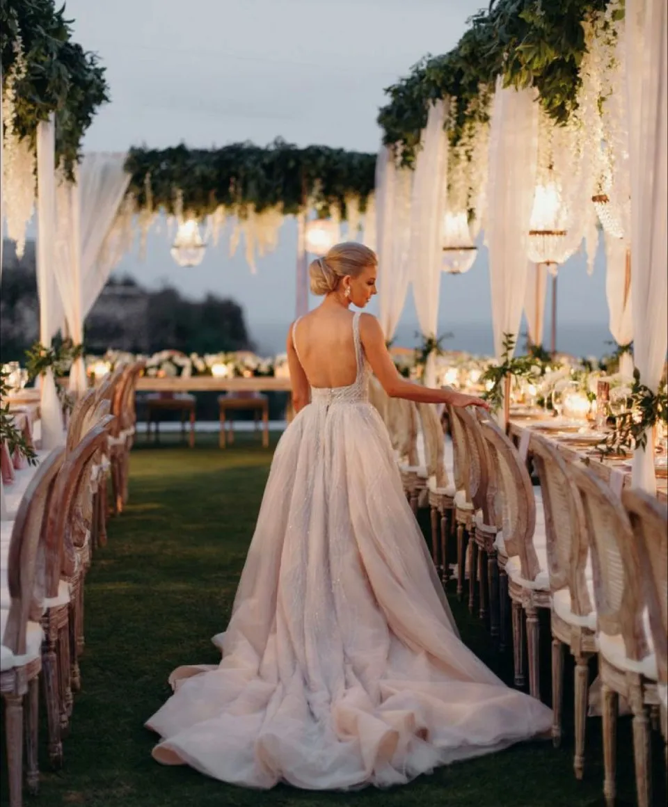 Bride in a blush gown standing among reception tables decorated with greenery