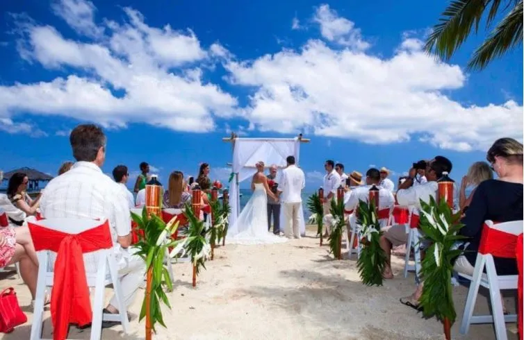 Beach wedding ceremony with guests seated on white chairs with red sashes in Roatán