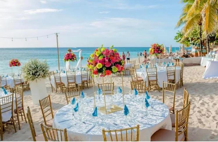 Beach wedding reception with round tables and colorful centerpieces by the sea in Roatán