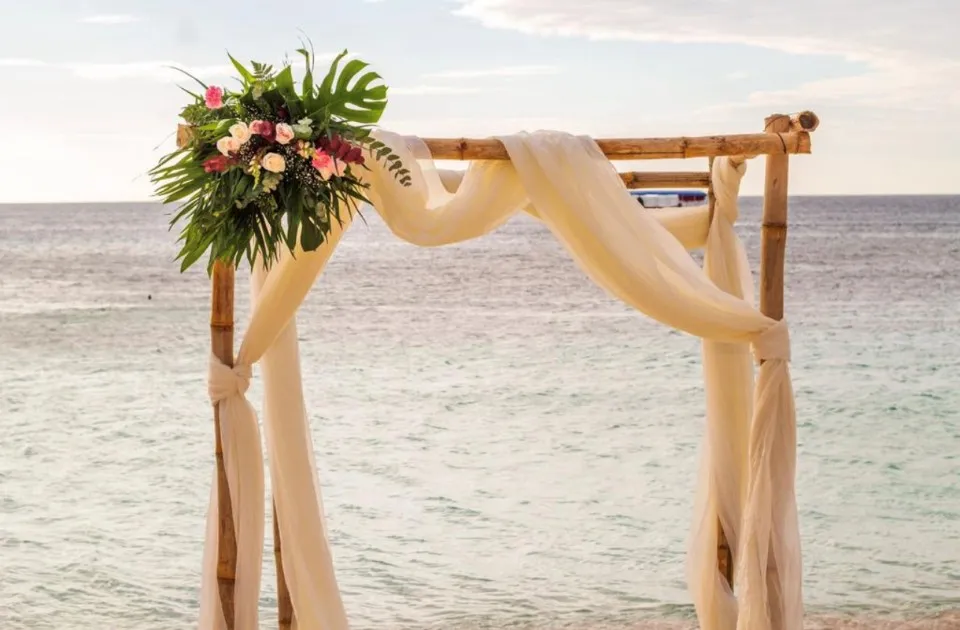 Bamboo wedding arch with ivory draping and tropical flowers on the beach