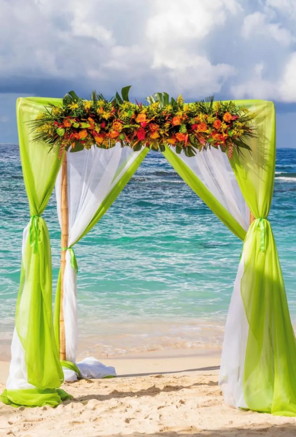 Wedding arch with lime green draping and tropical flowers on the beach