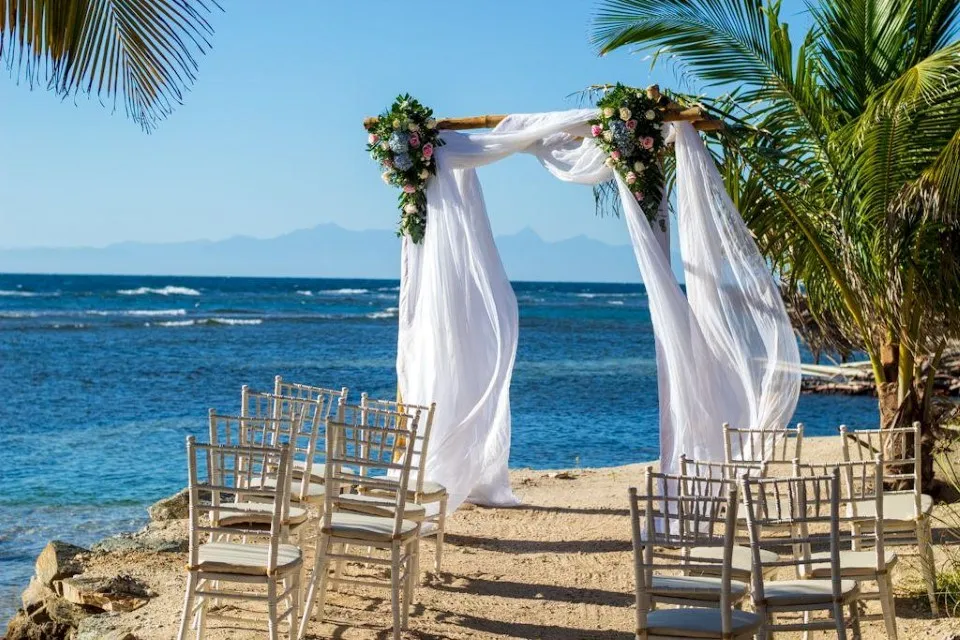White draped wedding arch and chairs on an oceanfront lawn in Roatán