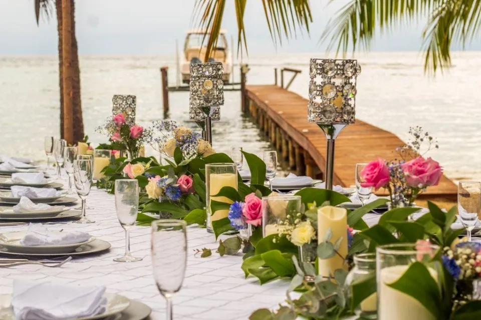 Wedding reception table with lanterns and flowers by a wooden dock on the beach