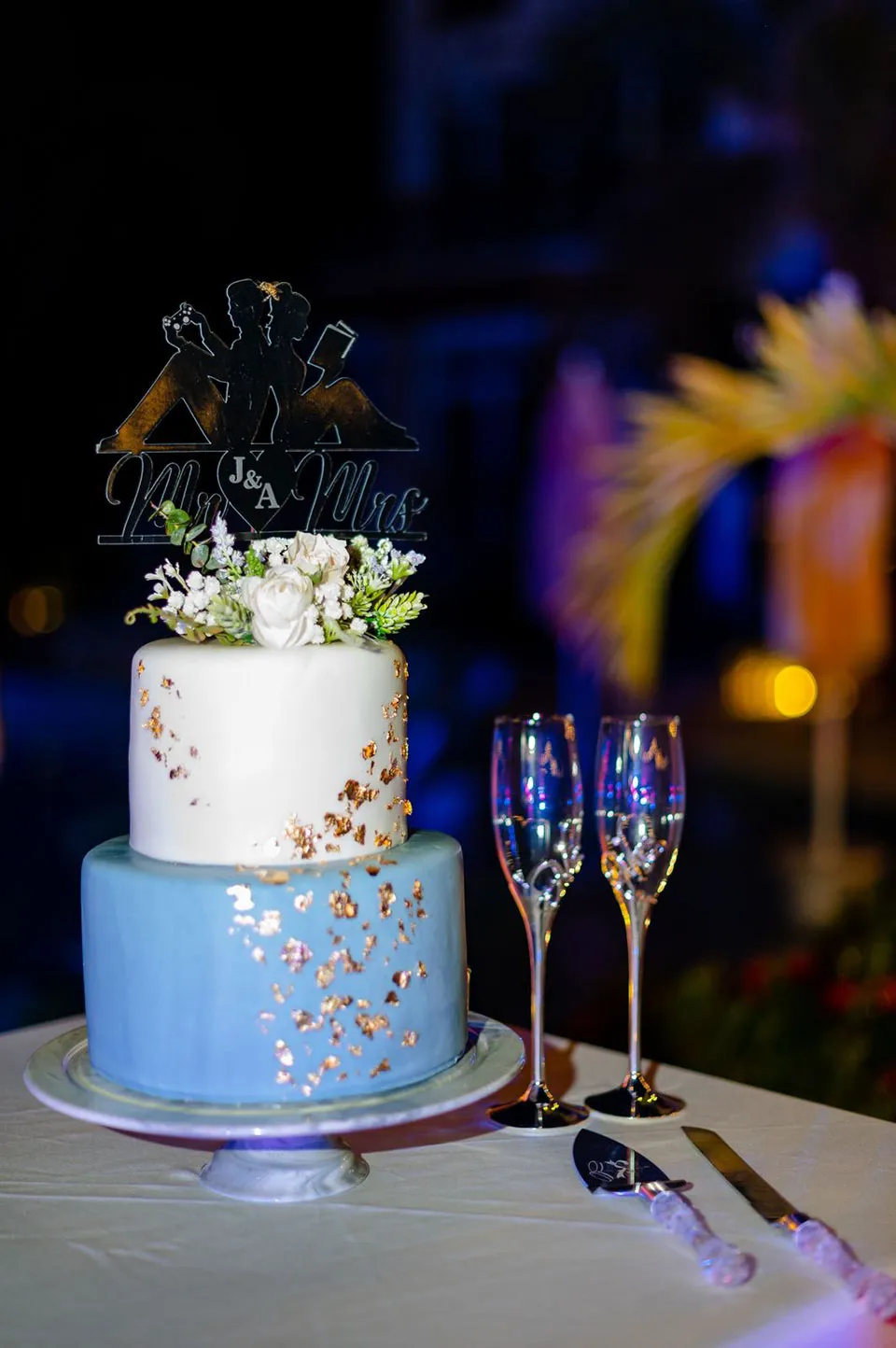 Two-tier blue and white wedding cake with flowers and champagne glasses