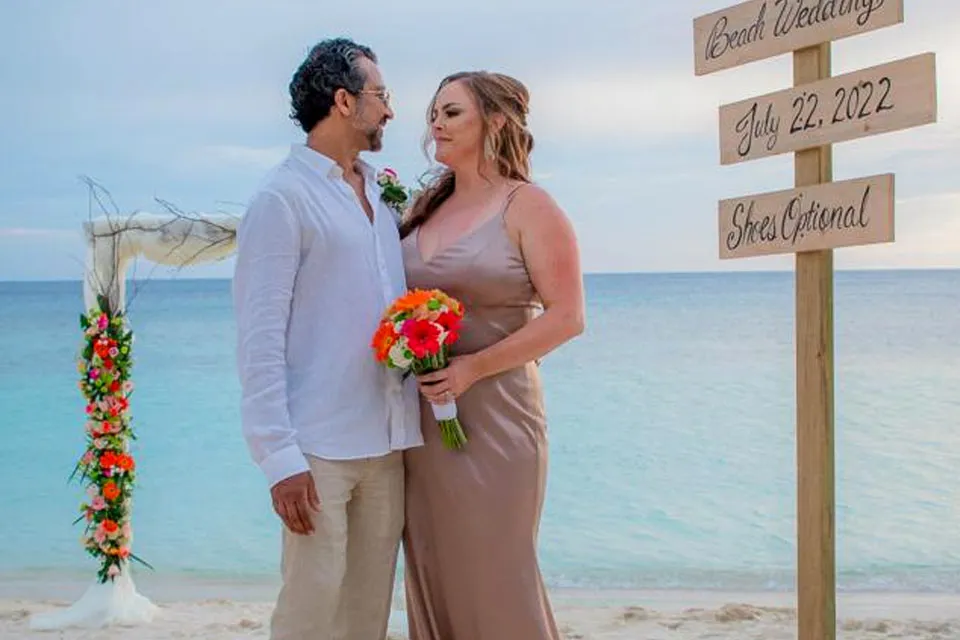 Couple holding a bouquet next to a wedding directional sign on the beach