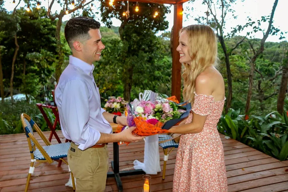 Man giving flowers to his girlfriend during a marriage proposal in Roatán
