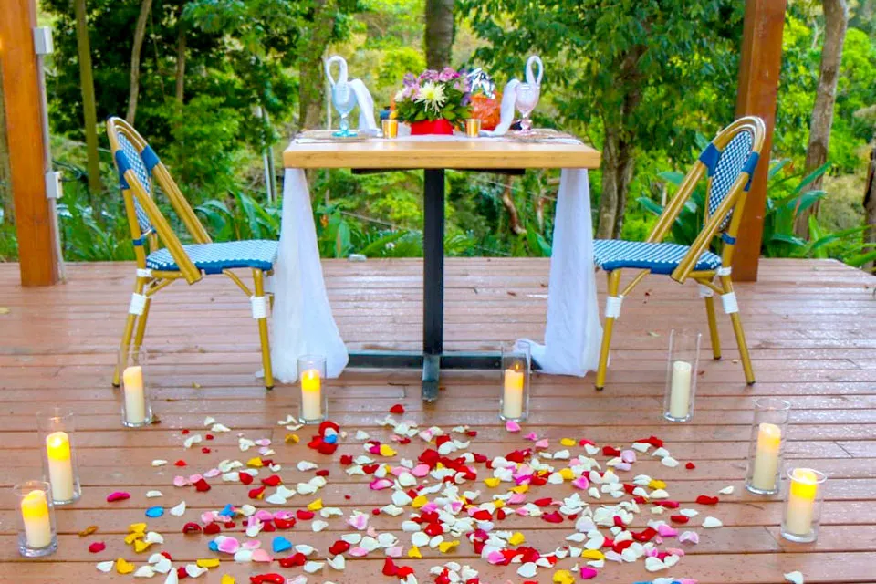 Romantic proposal table with candles and rose petals on a deck in Roatán