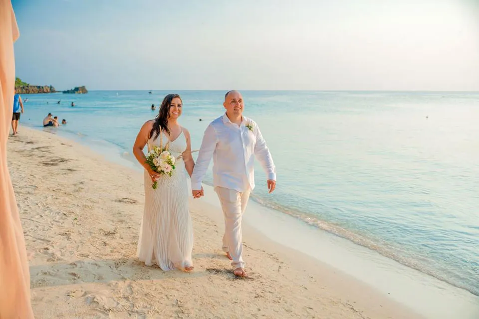 Bride and groom walking along the beach on a sunny day in Roatán