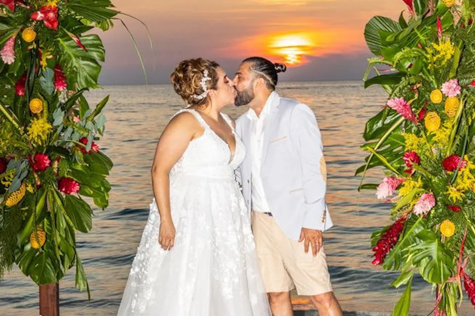 Couple kissing between tropical floral arrangements at sunset by the sea