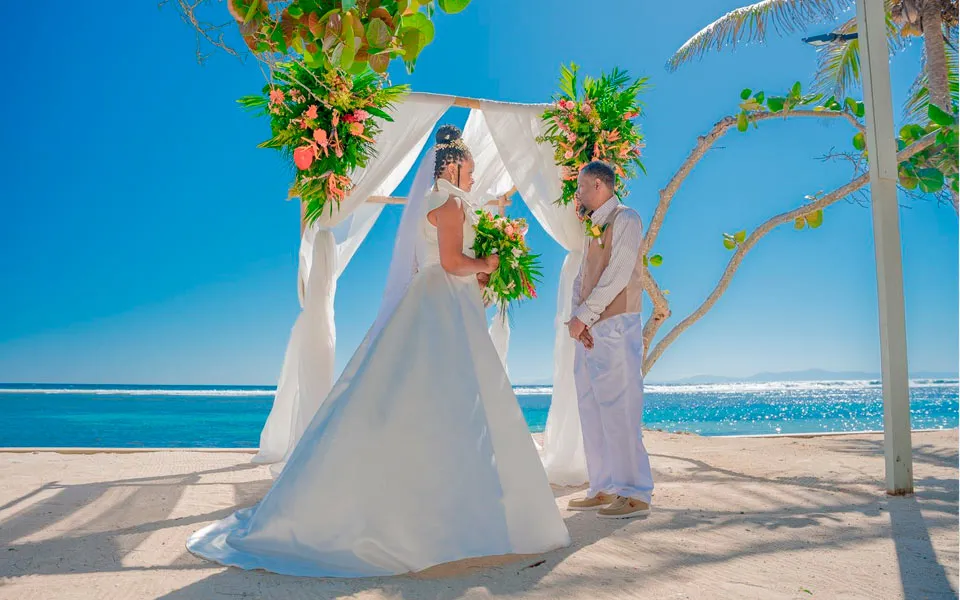 Bride and groom at a white draped arch on the beach during a cruise wedding in Roatán