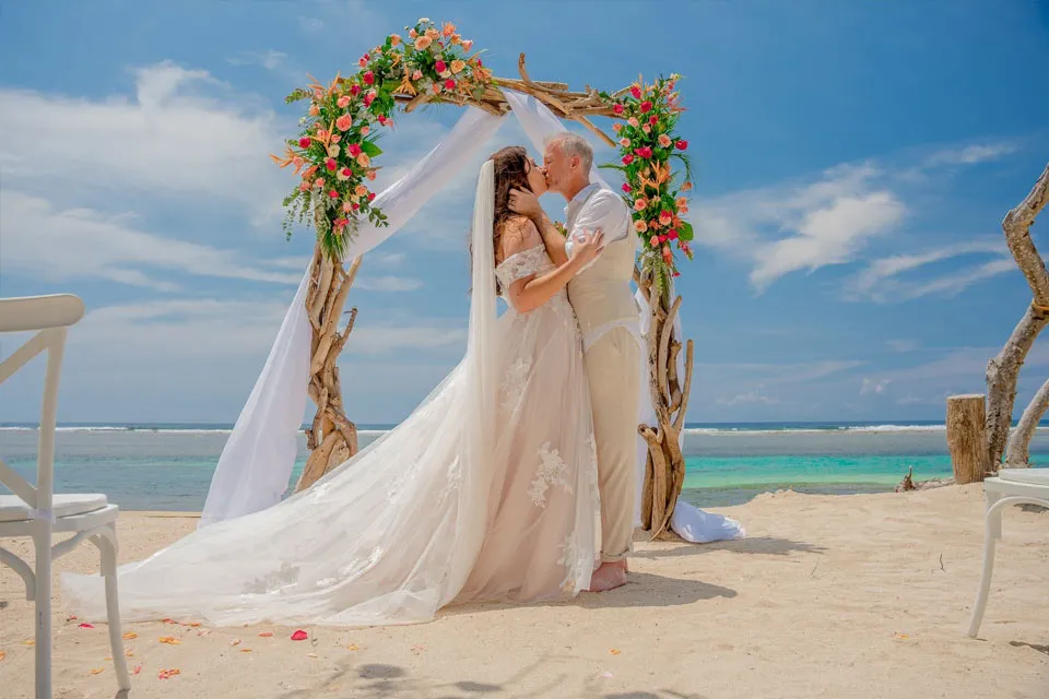 Couple kissing under a floral arch at an affordable beach wedding in Roatán