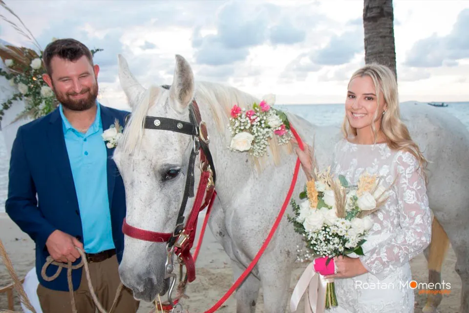 Bride and groom with a white horse decorated with flowers at Luna Beach Resort