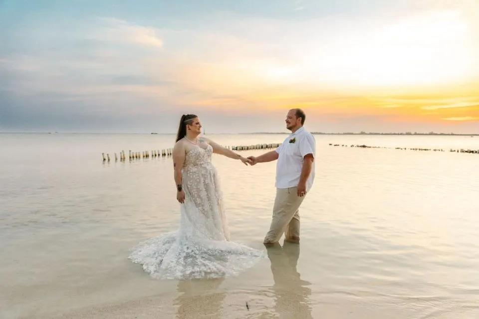 Bride and groom holding hands in the shallow sea at sunset at Bando Beach