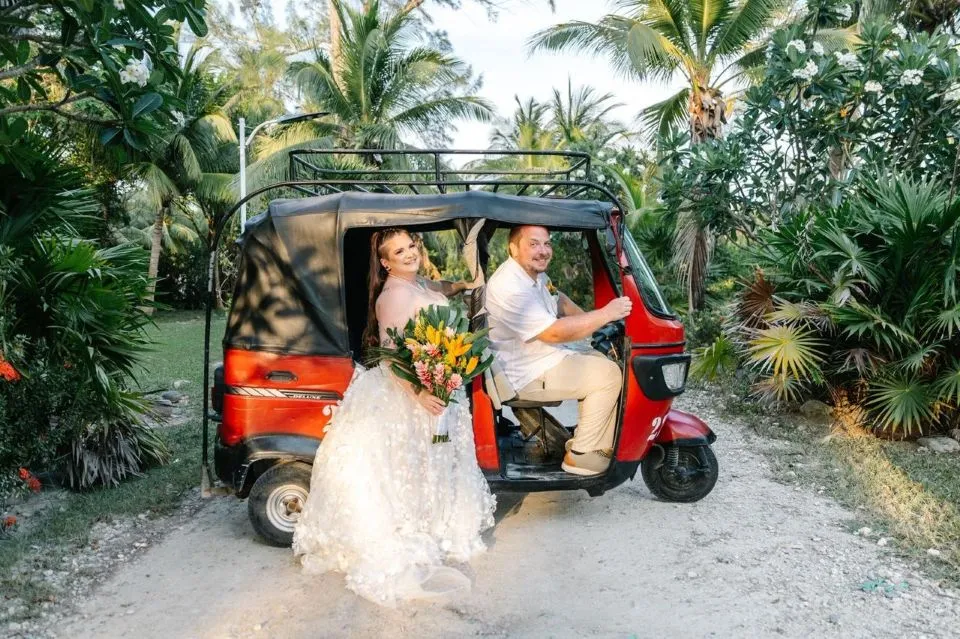 Bride and groom in a red tuk-tuk among palm trees in Utila