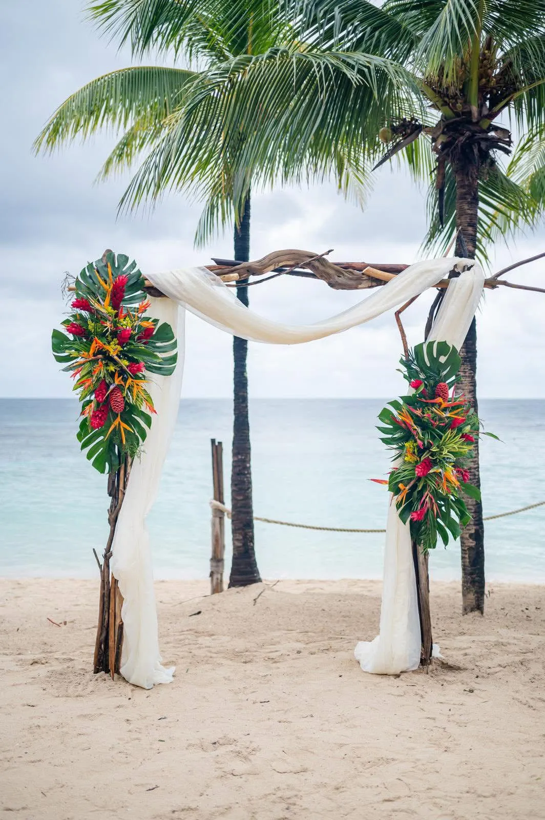 Draped wedding arch with tropical flowers between palm trees on the beach