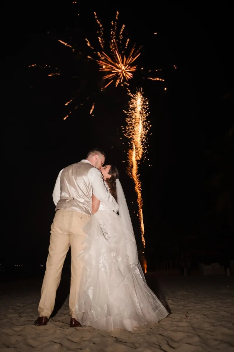 Bride and groom kissing under a fireworks sparkler at night on the beach