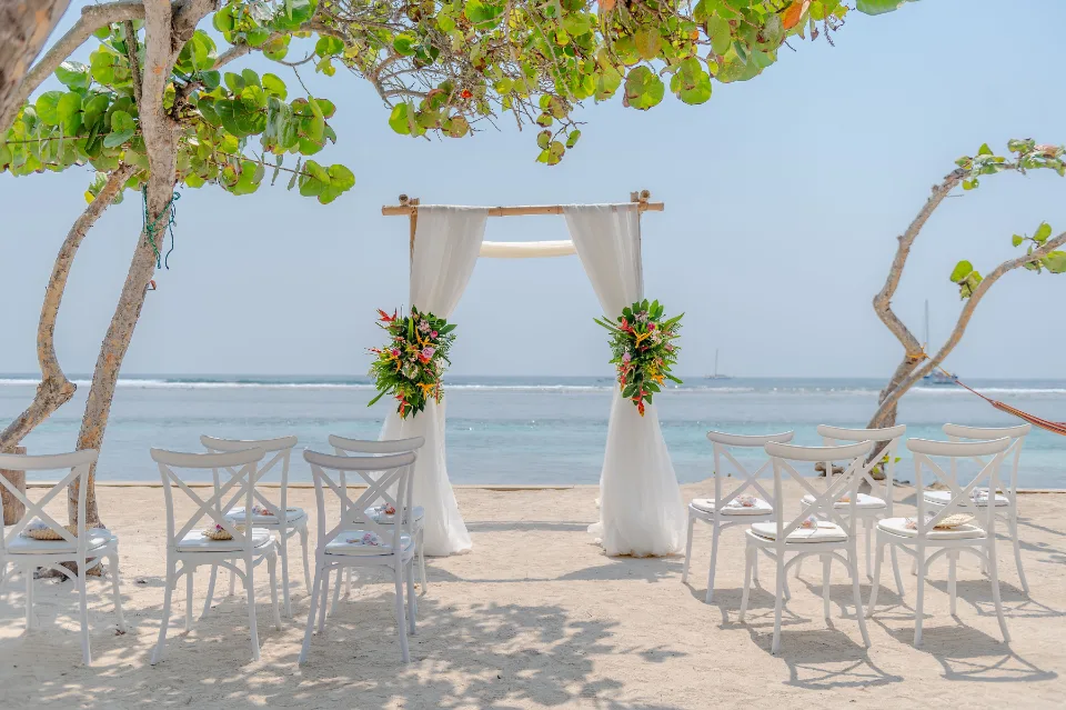 Intimate beach ceremony with white chairs and a draped bamboo arch in Roatán